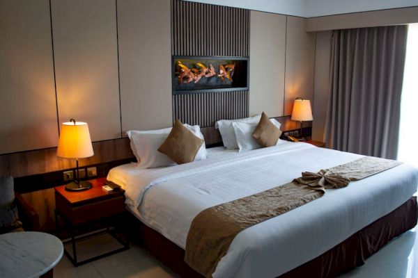 The image shows a modern hotel room with a neatly made bed, two bedside tables with lamps, and curtains partially covering the window.