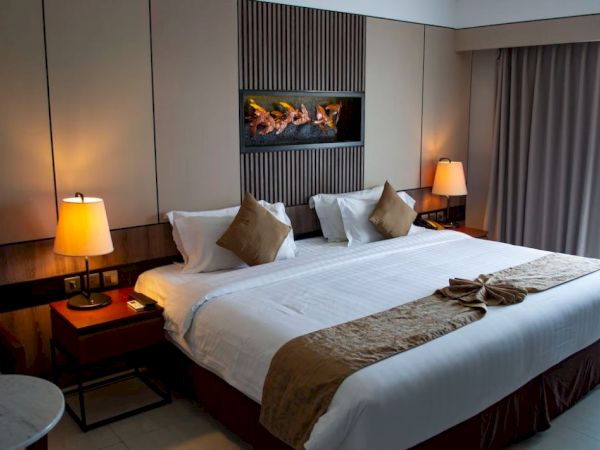 The image shows a modern hotel room with a neatly made bed, two bedside tables with lamps, and curtains partially covering the window.