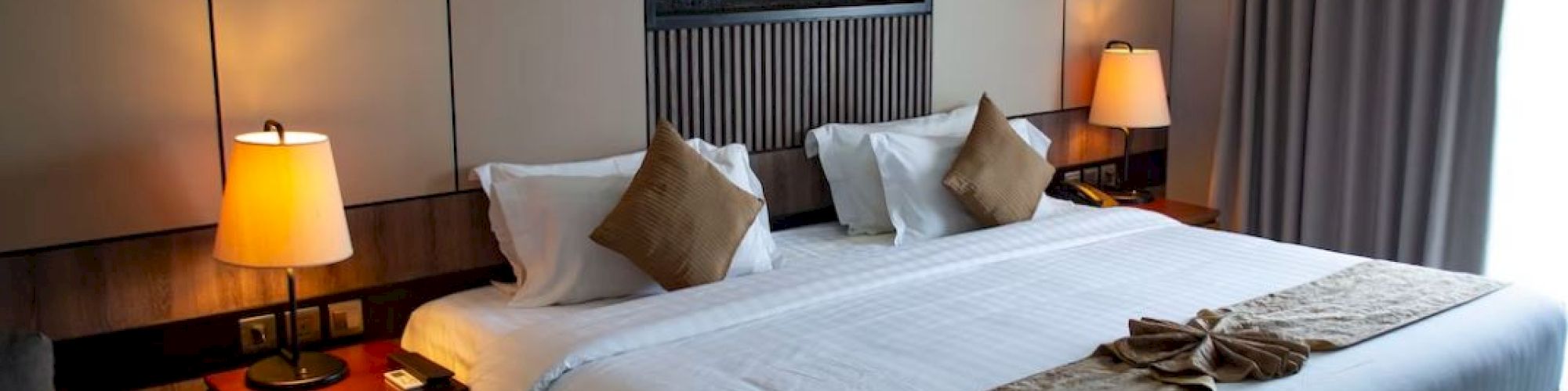 A cozy hotel room with a large bed, two bedside tables with lamps, a decorative fireplace, and a window with curtains.