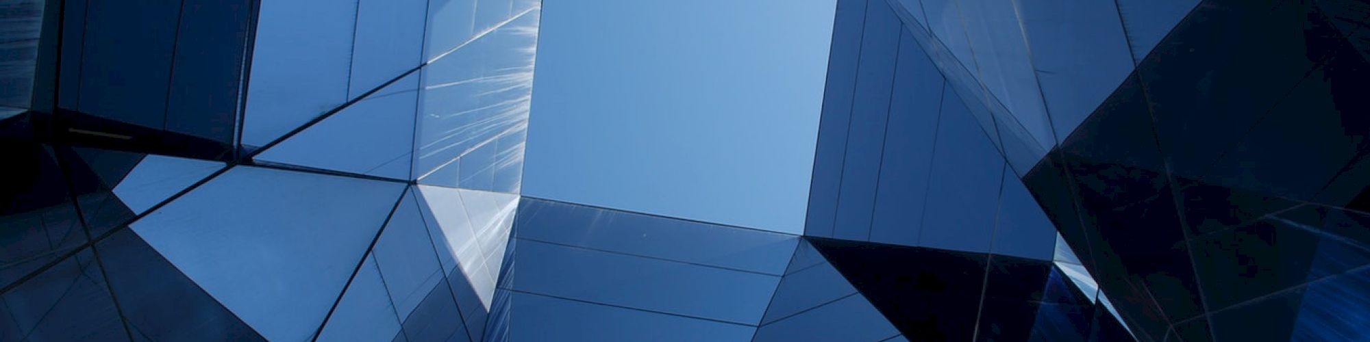 The image shows a geometric pattern of reflective glass buildings converging towards a clear blue sky, creating an abstract urban scene.