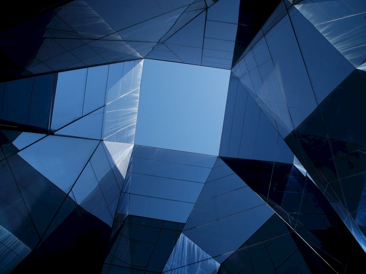 The image shows a geometric architectural structure with reflective glass panels, creating a symmetrical pattern under a clear blue sky.