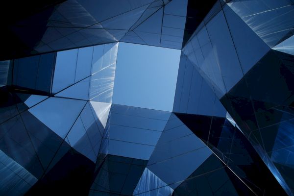 The image shows a geometric arrangement of glass and steel structures, forming a skylight through which a clear blue sky is visible.