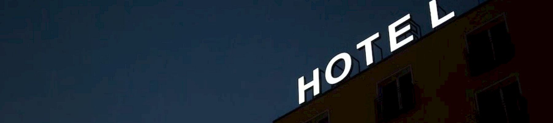 The image shows a building at night with an illuminated "HOTEL" sign, where the letter "H" is partially out, making it read "OTEL" on the top.