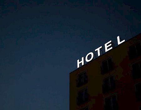 The image shows a building at night with an illuminated "HOTEL" sign, where the letter "H" is partially out, making it read "OTEL" on the top.