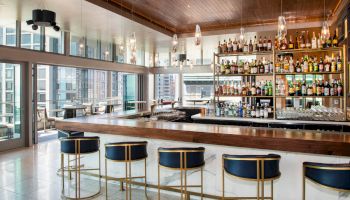 This image shows a modern bar with various alcoholic beverages on shelves, sleek bar stools, and large windows offering a city view, ending the sentence.