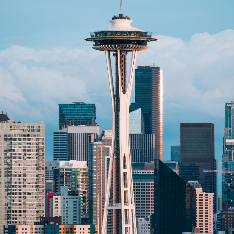 The image shows the Space Needle, an iconic observation tower in Seattle, with the city's downtown skyscrapers in the background against a cloudy sky.
