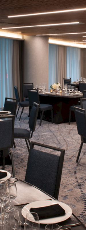 A banquet hall with round tables set with plates, glasses, and folded napkins, arranged for a formal event, featuring dim lighting and elegant decor.