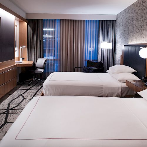 A modern hotel room featuring two neatly made beds, a flat-screen TV, a desk, and contemporary decor with a patterned wall and floor.