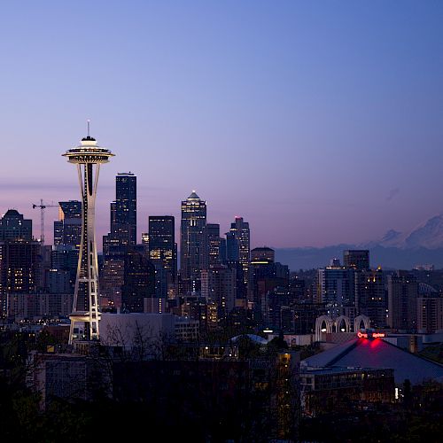This image shows the Seattle skyline at dusk, featuring the Space Needle prominently in the foreground and Mount Rainier visible in the background.