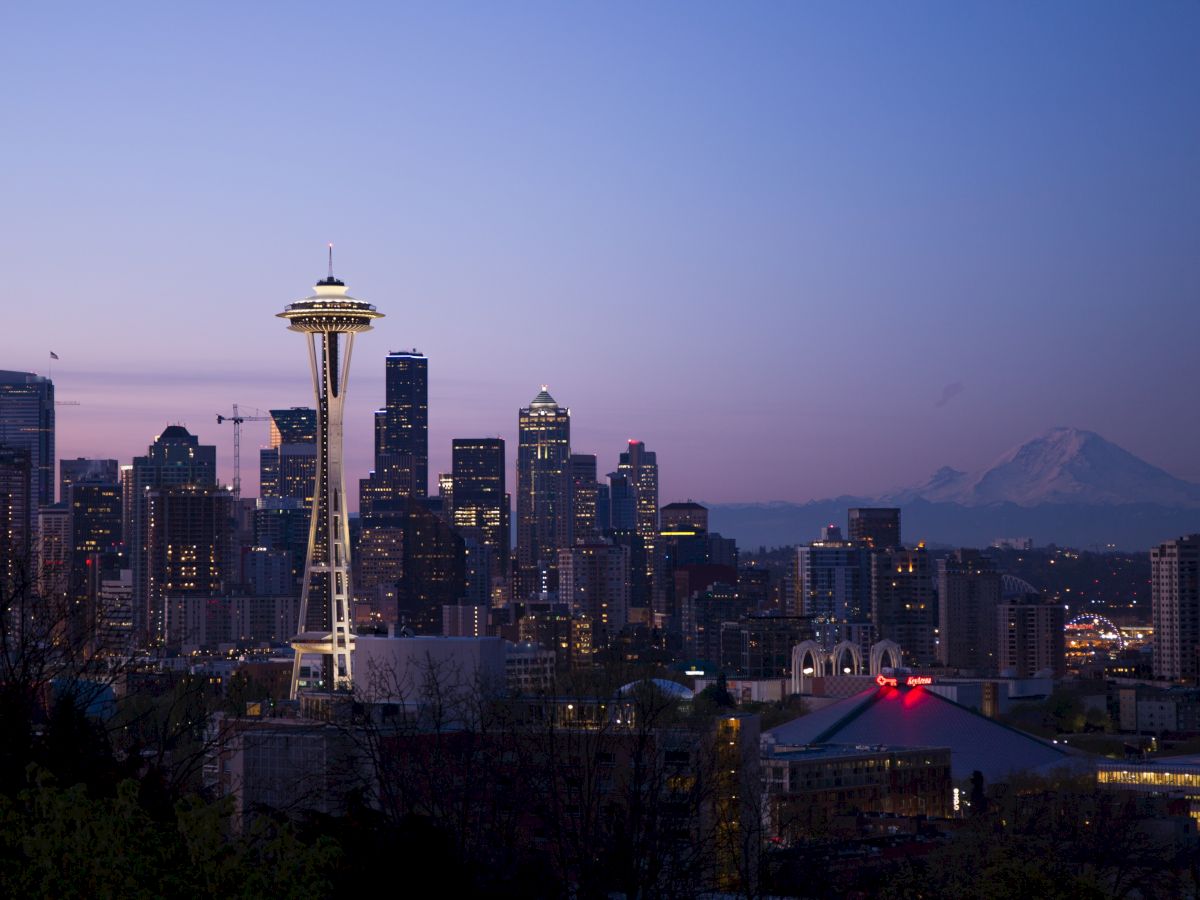 This image features the Seattle skyline at dusk, with the Space Needle prominently visible and Mount Rainier on the horizon in the background.