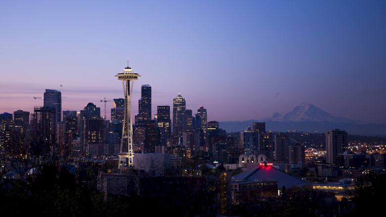 This image features the Seattle skyline at dusk, with the Space Needle prominently visible and Mount Rainier on the horizon in the background.